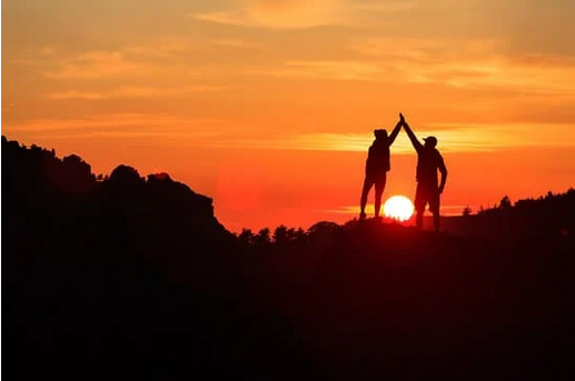 Two figures on a hill before a sunrise